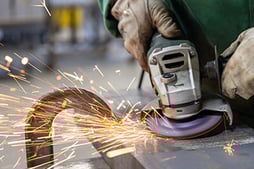 An operator removes mill scale from a workpiece with a bonded mill scale grinding wheel.