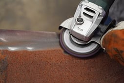 An operator uses a silicon carbide strip disc to remove rust for weld prep.