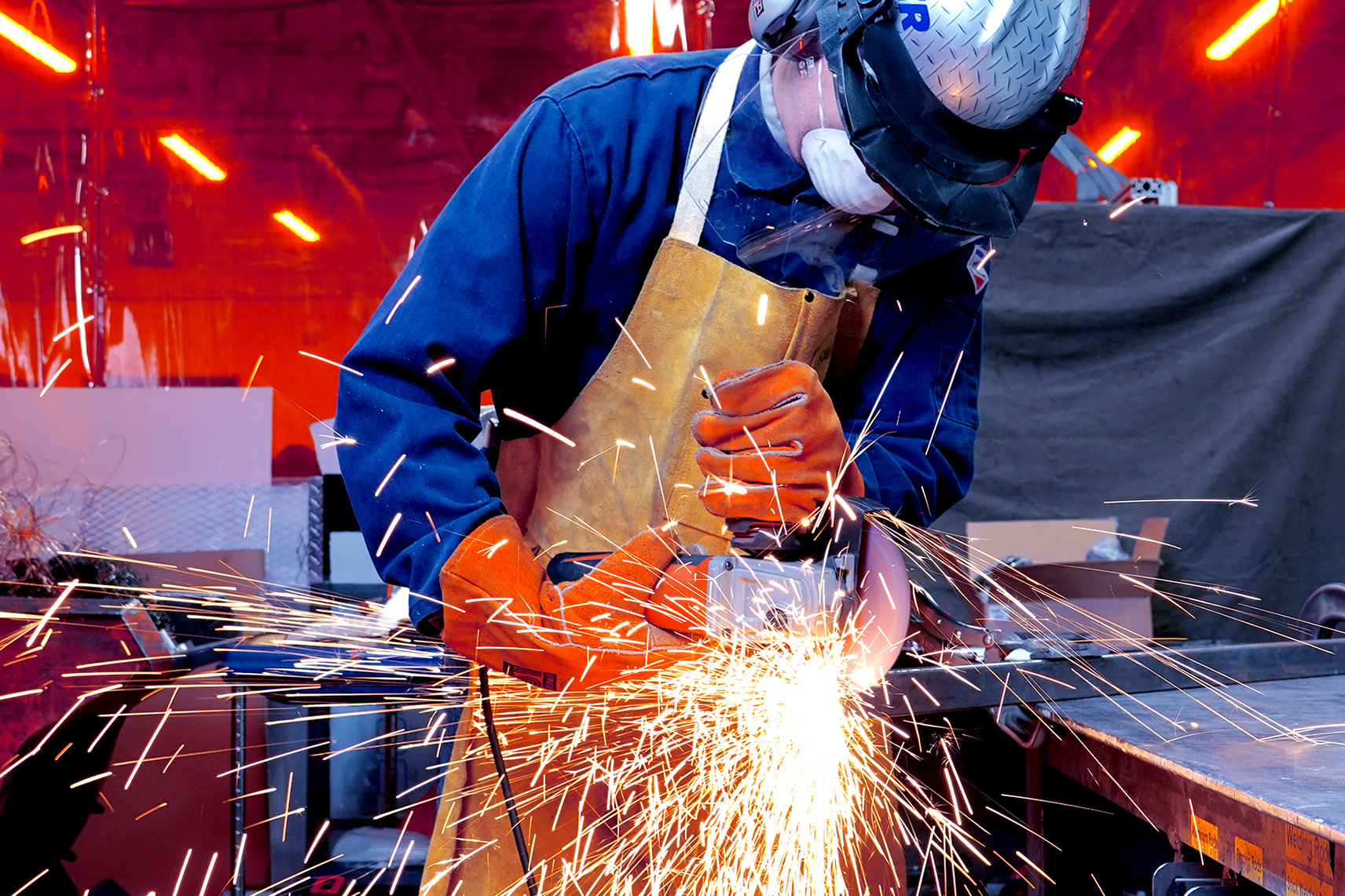 Experto en metalurgia con equipo de protección completo utilizando una amoladora angular y una rueda de corte para cortar acero